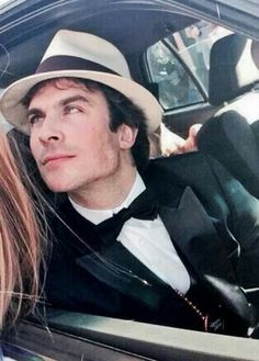 a man in a suit and tie sitting next to a woman in a car wearing a hat