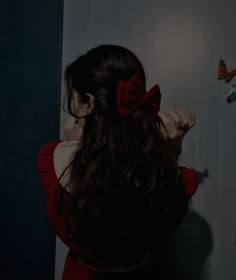 a woman in a red dress is holding her hair back and looking at a butterfly on the wall