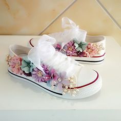 a pair of white shoes with flowers and pearls on the side, sitting on top of a table