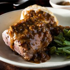 a white plate topped with meat covered in gravy and green beans