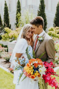 a bride and groom pose for a photo in front of a building with colorful flowers