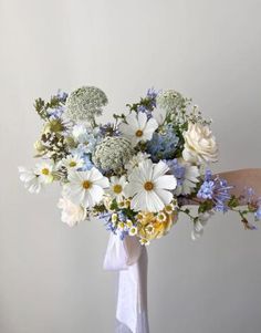 a bouquet of white and blue flowers is held by a woman's hand in front of a wall