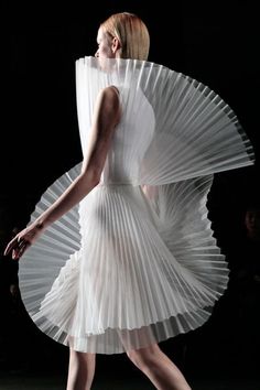 a woman is walking down the runway in a white dress with large pleated sleeves