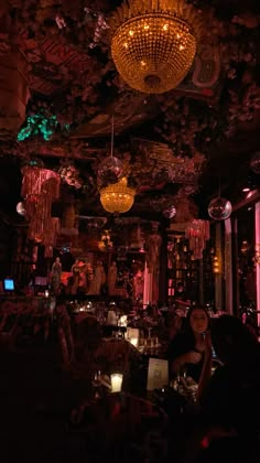 a dimly lit room with chandeliers hanging from the ceiling and people sitting at tables