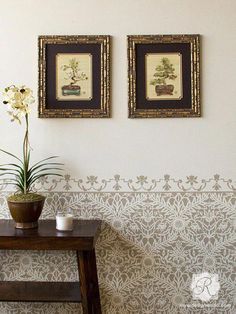 two framed pictures hang on the wall next to a table with a vase and candle