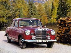 an old red car parked on the side of a road next to some trees and logs