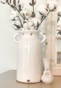 a white vase filled with cotton sitting next to a mirror