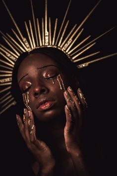 a woman with gold makeup and nails holding her hands up to her face in the dark