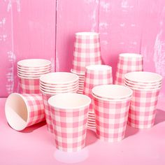 pink and white checkered paper cups are stacked on top of each other in front of a pink background