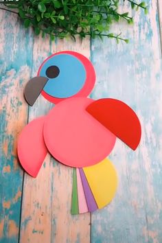 paper cut out of a pink bird on top of a wooden table with greenery in the background