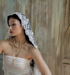 a woman in a wedding dress with a veil on her head and pearls around her neck