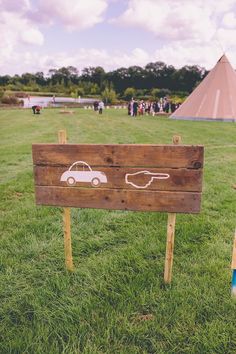 a wooden sign sitting on top of a lush green field next to a teepee