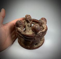 a hand holding a clay figurine with two people on it's back