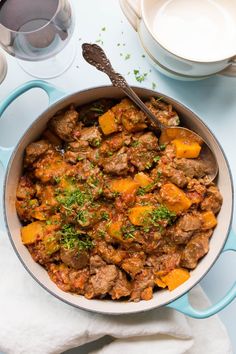 a pot filled with meat and vegetables on top of a blue table cloth next to white dishes