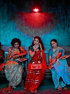 three women are sitting on a bench and one is holding a cell phone to her ear