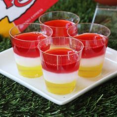 four glasses filled with jello sitting on top of a white plate in the grass