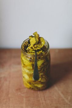 a jar filled with pickles sitting on top of a wooden table next to a spoon