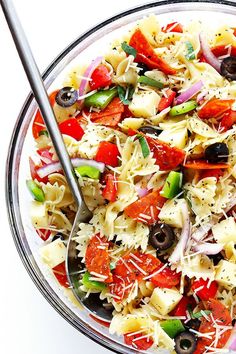 a glass bowl filled with pasta salad on top of a white table next to a spoon