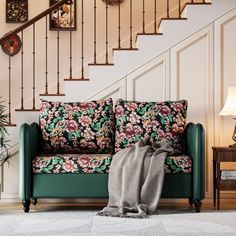 a green couch sitting under a stair case next to a table with a lamp on it