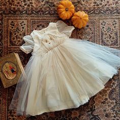 a white dress sitting on top of a rug next to two pumpkins and a book