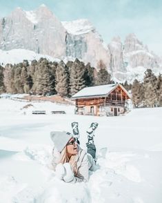 a woman laying in the snow with skis on her feet and mountains in the background