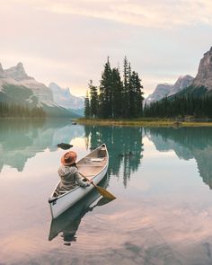 a person in a canoe paddling on the water with mountains and pine trees in the background