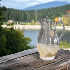 a pitcher filled with liquid sitting on top of a wooden table next to a lake