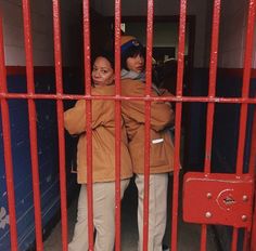 two women are standing behind bars in a jail cell, one is wearing an orange jacket