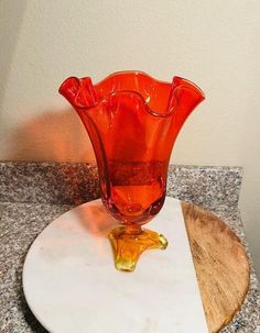 an orange glass vase sitting on top of a white plate next to a wooden cutting board