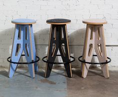 three stools are lined up against a white brick wall, one is black and the other is blue