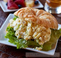 a sandwich with chicken salad on it sitting on a white plate next to some fruit