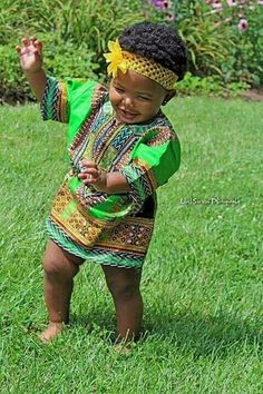 a baby standing in the grass wearing a headband and green shirt with yellow flowers on it's head