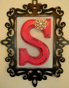 the letter s is painted red and black with a gold brooch on it's side