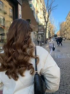 a woman with long brown hair is standing on the street