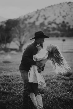 black and white photograph of a man kissing a woman in a field with mountains in the background