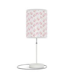 a white table lamp with pink flowers on the lampshade and an electric plugged in