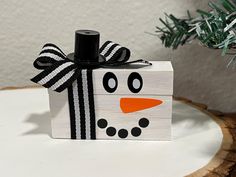 a wooden block with a black and white snowman design on it sitting next to a christmas tree