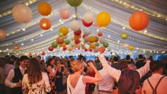 a group of people standing under a tent with paper lanterns hanging from it's ceiling