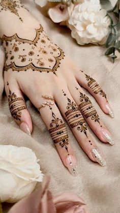 a woman's hand with henna tattoos on it and flowers in the background