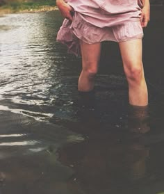 a woman standing in the middle of a river wearing a pink dress and holding an umbrella