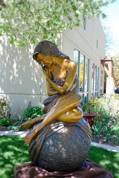 a statue of a woman sitting on top of a rock in the grass next to a building