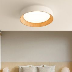 a bed with white sheets and pillows under a round light fixture on the wall above it