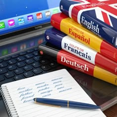 a stack of books sitting on top of a laptop computer next to a pen and notebook