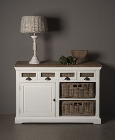 a white sideboard with wicker baskets and a lamp