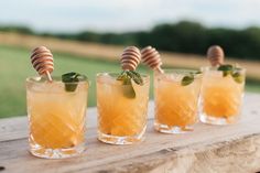 three glasses filled with drinks sitting on top of a wooden table next to each other