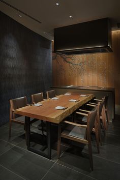 a long wooden table with chairs around it in front of a black wall and wood paneling