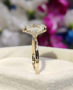 a diamond ring sitting on top of a white cloth with flowers in the back ground