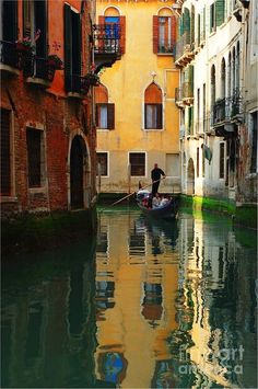 a person on a small boat in the middle of a canal with buildings and balconies