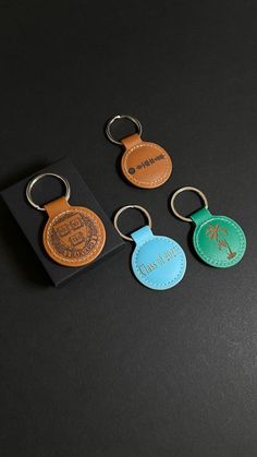 four different colored leather keychains on a black surface, one has a tag and the other has a logo