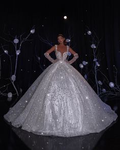 a woman in a white dress standing next to some trees and lights on the ground